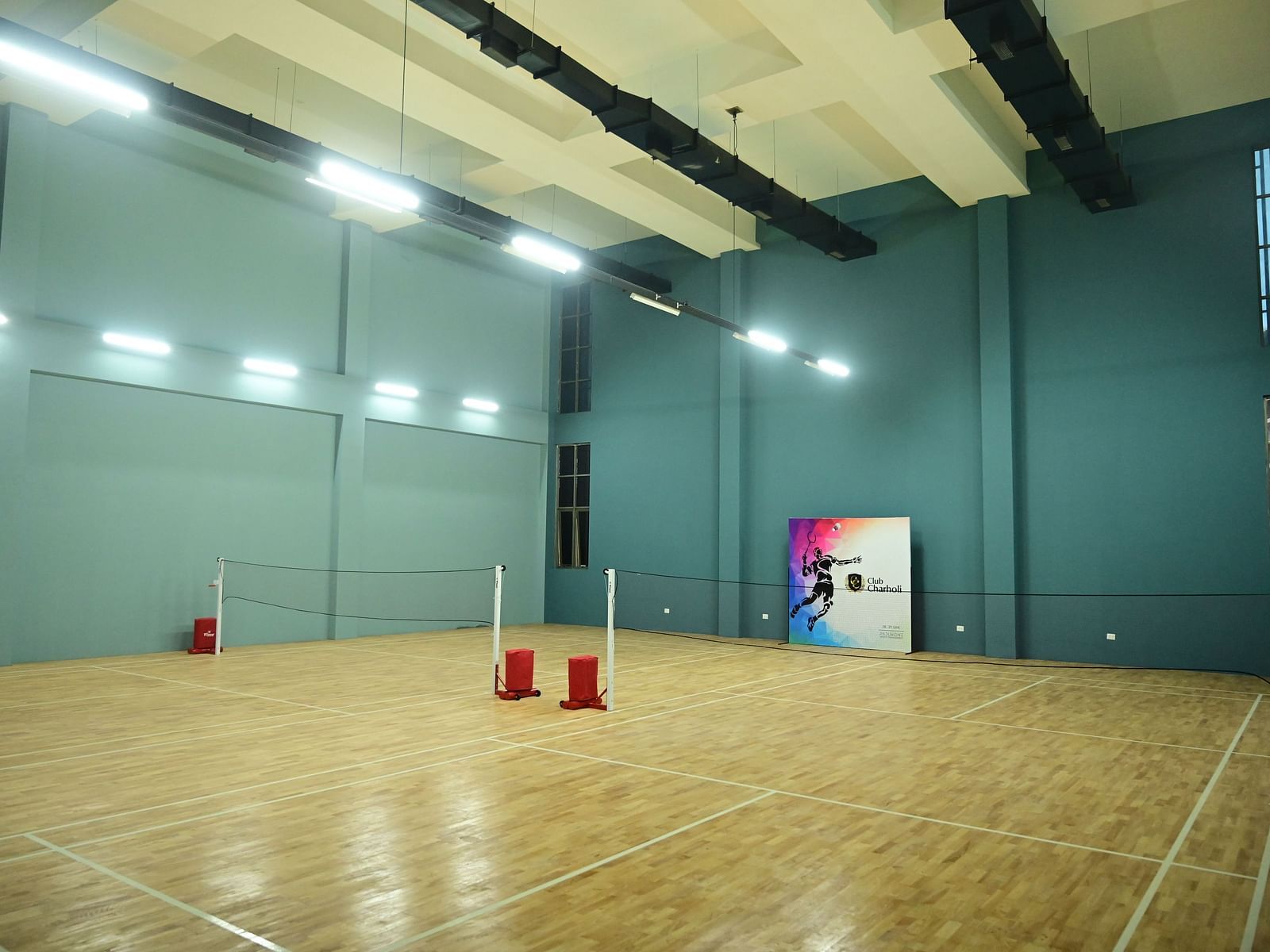 an indoor badminton court with teal coloured walls at club charholi, pune